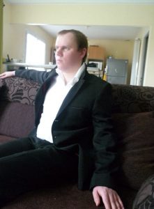 Nicolas Braconnier portant un costume noir et une chemise blanche est assis dans un canapé d'angle.